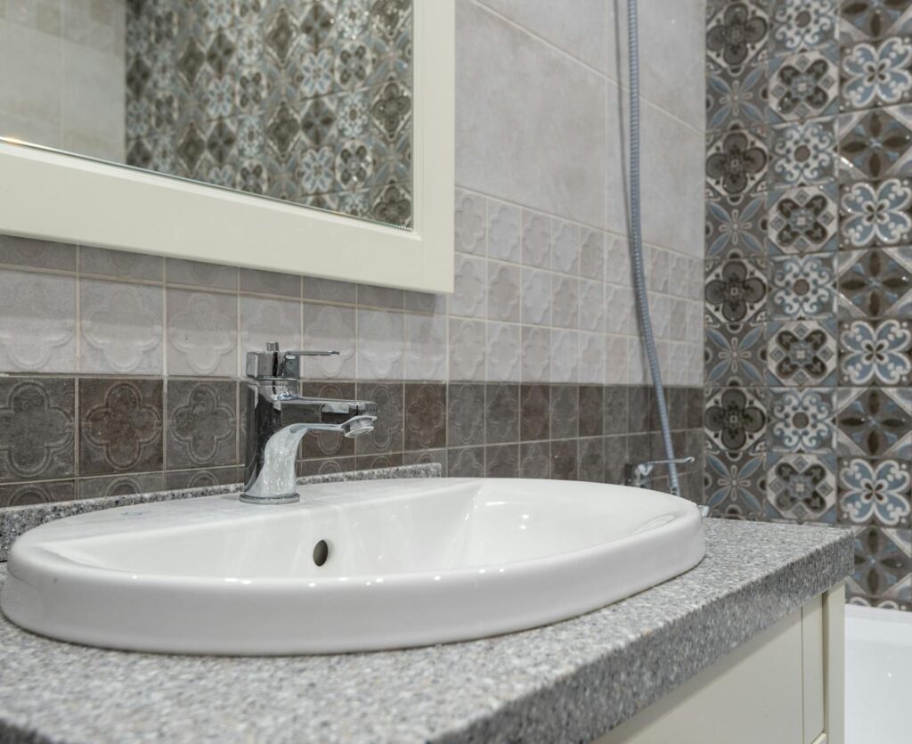 Close-up of a modern white sink and faucet with ornate patterned tiles in the bathroom.